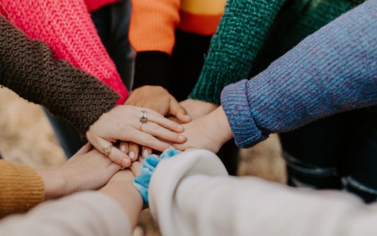 Menschen mit verschiedenen Pullovern legen ihre Hände in der Mitte zusammen.